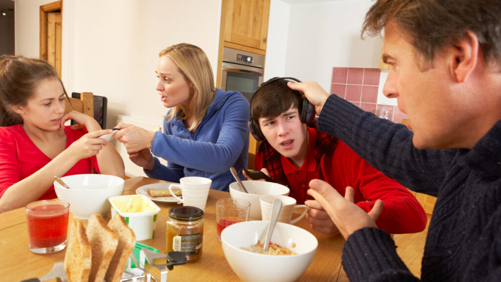Unhappy Family at kitchen table having breakfast while children are using devices.