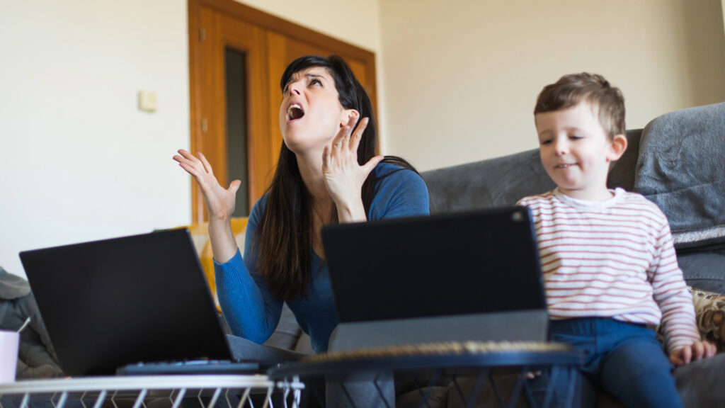 Frustrated mom using laptop and child using tablet.